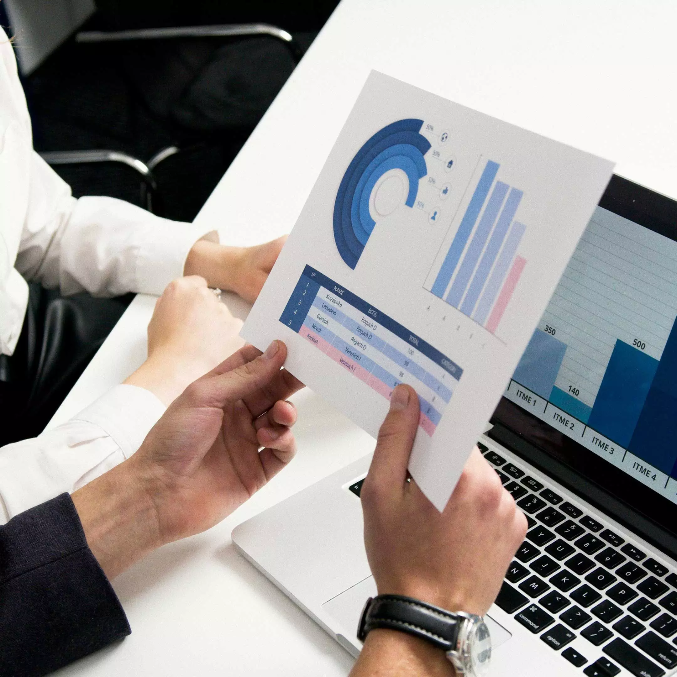 Image of two people sitting at a desk reviewing financial data printed on a piece of paper with a laptop within reach